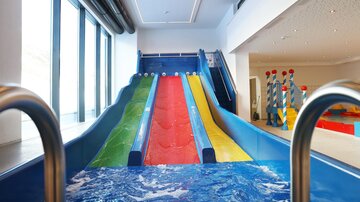 Ein Indoor-Wasserpark mit mehreren Wasserrutschen in bunten Farben. Im Vordergrund ist das Wasserbecken sichtbar, das unter den Rutschen liegt.