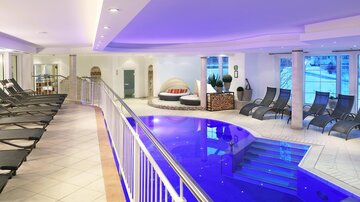 Ein modernes Spa mit einem blauen Pool und Liegen. Der Bereich ist hell und einladend gestaltet.