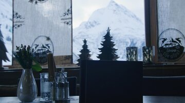 Ein gemütliches Restaurant mit Blick auf schneebedeckte Berge. Auf dem Tisch stehen eine Blumenvase und Gewürzstreuer.