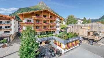 Ein charmantes Bergdorf mit traditionellen Holzhäusern und einer malerischen Landschaft. Im Vordergrund sind gemütliche Terrassen und Grünflächen zu sehen. | © Rössle