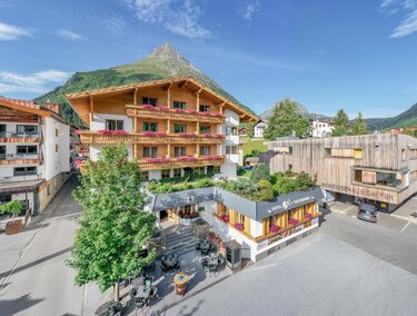 Ein charmantes Bergdorf mit traditionellen Holzhäusern und einer malerischen Landschaft. Im Vordergrund sind gemütliche Terrassen und Grünflächen zu sehen. | © Rössle
