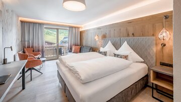 Ein modernes Hotelzimmer mit zwei Betten, einer gemütlichen Sitzecke und Blick auf die Natur. Die warme Holzverkleidung sorgt für eine einladende Atmosphäre.