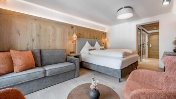 Ein modernes Zimmer mit einem großen Bett und gemütlichen Sitzmöbeln. Die warmen Farben und Holzdetails schaffen eine einladende Atmosphäre.