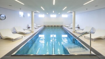Ein modernes Schwimmbad mit klarem Wasser und Liegen. Die Wände sind hell und die Beleuchtung ist freundlich. | © Rössle