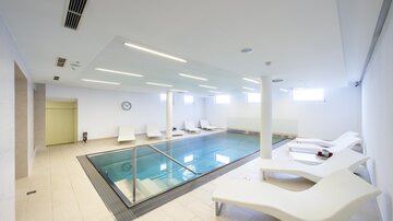 Ein modernes Hallenbad mit einem glasklaren Wasser und bequemen Liegen. Der Raum ist hell und minimalistisch gestaltet. | © Rössle