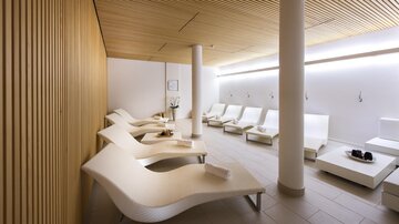 Ein moderner Wellnessbereich mit eleganten Liegen und sanfter Beleuchtung. Die Wände sind aus hellem Holz und der Raum strahlt Ruhe aus. | © Rössle