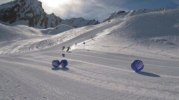 Eine verschneite Berglandschaft mit Skifahrern auf der Piste. Im Vordergrund sind blaue Kugeln zu sehen, die Teil des Skigebiets sind.