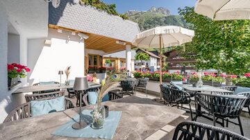 Eine gemütliche Terrasse mit runden Tischen und Stühlen. Im Hintergrund sind Pflanzen und Berge zu sehen, bei sonnigem Wetter. | © Rössle