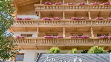 Ein schönes Hotel mit Holzverkleidung und blühenden Balkonen. Der Eingang ist einladend und von Pflanzen umgeben.