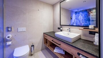 Ein modernes Badezimmer mit einem großen Spiegel und einem eleganten Waschbecken. Die Wände sind in neutralen Farben gehalten, und es gibt Holzdetails.