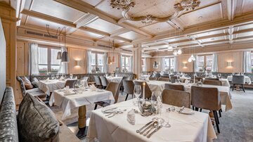Ein elegantes Restaurant mit stilvollen Tischen und Stühlen. Die Decke ist kunstvoll verziert und das Ambiente ist gemütlich.