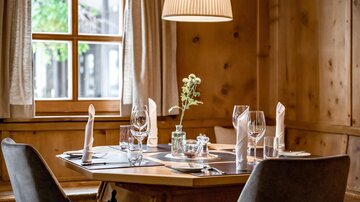 Ein einladender Tisch in einem gemütlichen Restaurant. Er ist mit Gläsern, Besteck und einer kleinen Blumendekoration gedeckt.