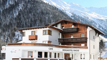 Ein charmantes Berghotel mit einem Café, umgeben von schneebedeckten Bergen. Die klare Winterlandschaft sorgt für eine einladende Atmosphäre.