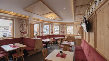 Ein gemütliches Restaurant mit Holzverkleidung und roten Sitzen. Die Fenster bieten einen Blick nach draußen und es gibt Tische für Gäste.
