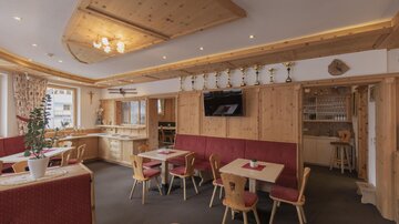 Ein gemütliches Restaurant mit Holzdekor und roten Polstermöbeln. Es gibt Tische mit Stühlen und eine Bar im Hintergrund.