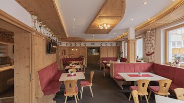 Ein gemütliches Restaurant mit Holzdekor und roten Polsterbänken. Die Tische sind schlicht gedeckt, und es gibt eine warme, einladende Atmosphäre.