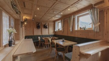 Ein gemütliches Restaurant mit Holzwänden und -möbeln. Es gibt Tische und Bänke, sowie Fenster mit Ausblick auf die Berge.