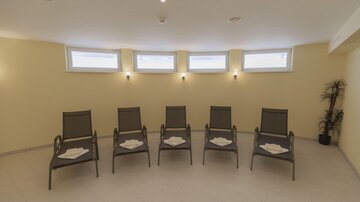 Ein entspannender Raum mit fünf Liegestühlen und hellem, wärmem Farbton. Große Fenster sorgen für natürliches Licht.