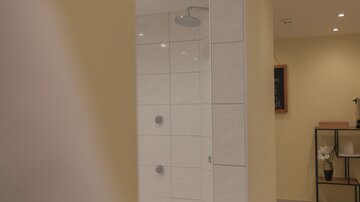 Eine moderne Dusche mit weißen Fliesen in einem gelben Raum. Im Hintergrund sind dekorative Elemente und sanfte Beleuchtung zu sehen.