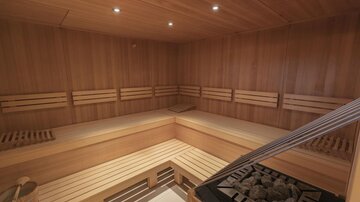 Eine moderne Sauna mit Holzbank und sanfter Beleuchtung. Der Raum ist einladend und bietet einen Ort der Entspannung.