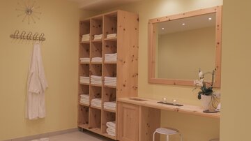 Ein entspannender Wellnessbereich mit gelben Wänden und Holzregalen. Faltige Handtücher und ein großer Spiegel schaffen eine ruhige Atmosphäre.