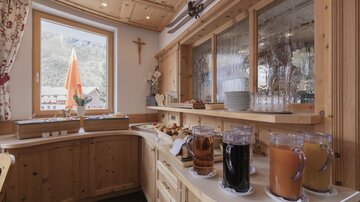 Ein gemütlicher Essbereich mit Holzverkleidung, einer Fensteransicht und einem Buffet. Auf der Theke stehen verschiedene Getränke und frische Brötchen bereit.