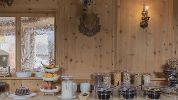 Ein gemütliches Frühstücksbuffet mit verschiedenen Früchten, Joghurt und Cerealien. Die Holzwände und die dekorativen Elemente schaffen eine warme Atmosphäre.