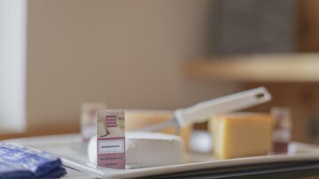 Eine Auswahl an Käsesorten auf einem Tisch. Dazu ein Käsemesser und einige Käsebeschreibungen.