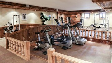 A modern gym with various equipment. The walls are lined with wood and there are large windows for natural light.