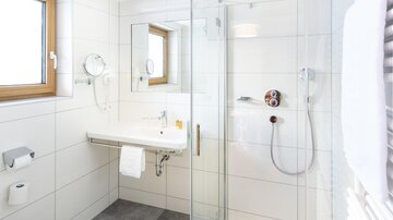 A modern bathroom with a glass shower and bright tiles. There is a window and a sink shelf.
