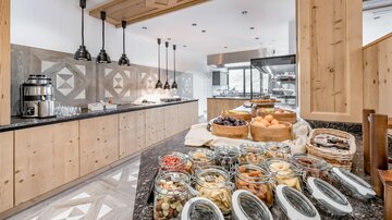 A modern kitchen with wood paneling and elegant pendant lights. Various glasses with snacks and baked goods are arranged on the table.