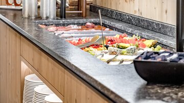An inviting buffet with fresh vegetables, fruit, and cold cuts. The area is designed in a wooden, modern style.