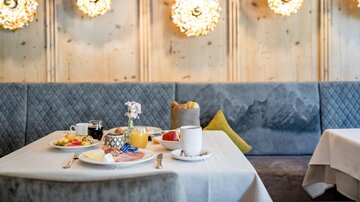 An elegant breakfast table with various dishes, including fruit and pastries. The wall is decorated with stylish light sources that create a cozy atmosphere.