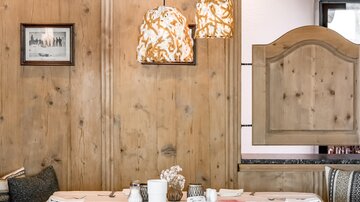 A stylish restaurant with wood-paneled walls and modern pendant lights. The table is elegantly set, creating an inviting atmosphere.