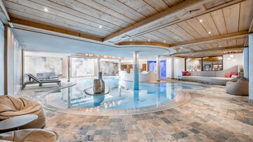 A modern swimming pool in a stylish interior with a wooden ceiling. Comfortable seating and a relaxing area invite you to linger.