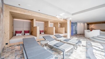 A modern wellness area with cozy loungers and wooden details. Daylight floods through large windows, creating a relaxing atmosphere.