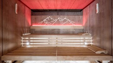 A modern sauna with a wooden bench and soft lighting. The wall features a stylized mountain landscape.