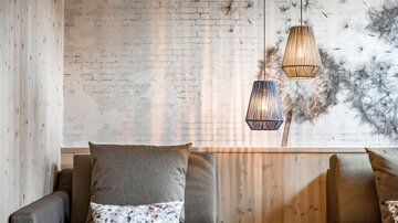 A stylish lounge with comfortable sofas and modern lamps. The walls are made of light wood and brick, creating an inviting atmosphere.