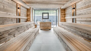 A modern sauna interior made of wood with comfortable benches. Large windows provide a view outside and let in plenty of light.