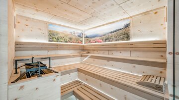 A modern sauna with wooden benches and soft lighting. Landscape images adorn the walls, creating a relaxing atmosphere.