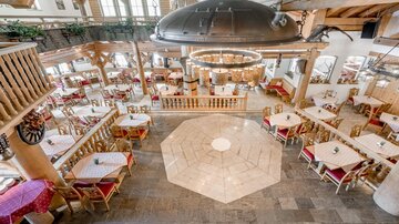 A cozy restaurant with wooden decor and many tables. The relaxed atmosphere is complemented by large windows and elegant lighting.