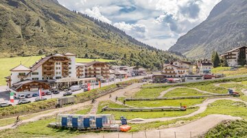 A picturesque mountain landscape with a small village and green meadows. Nearby, there are recreational activities such as a dirt bike track.