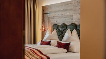 A stylish bedroom with a cozy double bed and a modern wooden headboard. The warm colors and decorative cushions create an inviting atmosphere.