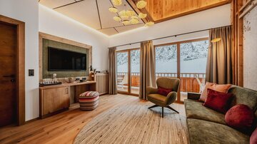 A cozy living space with modern furniture and large windows overlooking a snow-covered landscape. The warm wood and color tones create an inviting atmosphere.